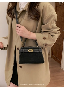 Detail of black suede crossbody bag with gold hardware and contrast stitching on trench coat