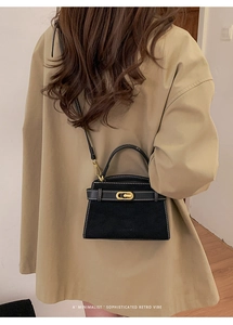 Detail of a retro black trapezoid handbag with white stitching and golden hardware