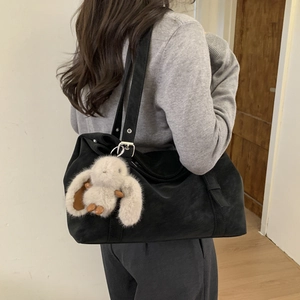 Detailed side view of a large black suede tote bag with a cute plush bunny pendant