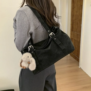 Detail of black faux suede tote bag with adjustable silver buckle strap and plush rabbit charm