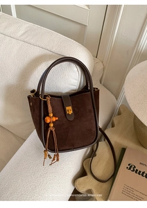 Detail der Vintage Wildleder-Beuteltasche in Braun mit dekorativer Holzquaste auf Sofa