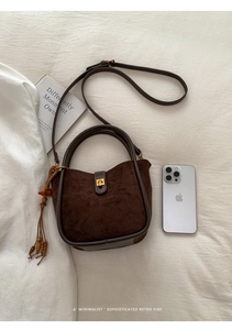 Detailansicht einer braunen Wildleder-Retro-Eimertasche mit Goldverschluss und Quaste