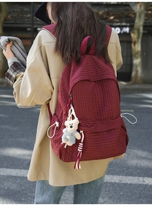 Side view of red plaid school backpack with cute bear pendant in an outdoor setting
