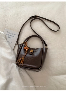 Details der dunkelbraunen Vintage-Lederhandtasche mit Holzperlenquaste und Goldbeschlägen