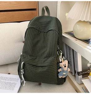 Detail of dark green plaid backpack with a cute teddy bear plush charm and white drawstrings