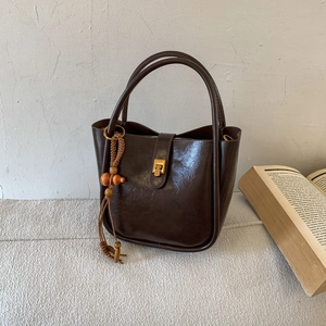Detailansicht der dunkelbraunen Eimertasche aus Kunstleder mit Goldschloss und Holzanhänger