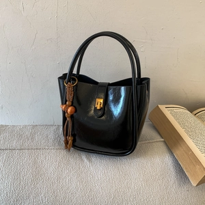Detail einer schwarzen Lackleder-Beuteltasche mit Goldbeschlägen und Quastenanhänger