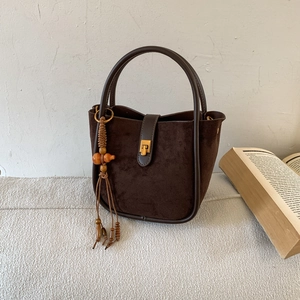 Detailansicht der dunkelbraunen Wildleder-Beuteltasche mit Ledergriffen und Retro-Anhänger