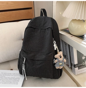Detail of black grid school backpack with plush bear charm and sturdy zippers
