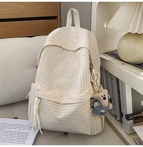 Detailed close-up of cream canvas striped backpack with cute bear pendant and side tag