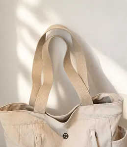 Dettaglio della tracolla larga in tessuto e fibbia metallica sulla borsa tote color crema