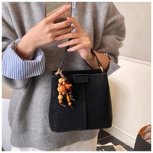 Dettaglio della borsa a secchiello nera opaca con ciondolo in legno e texture in pelle