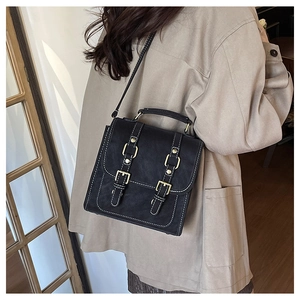 Détail du sac à dos en similicuir noir avec boucles dorées sur un trench-coat classique