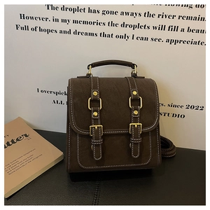 Détail du sac à dos rétro en cuir mat marron foncé avec surpiqûres blanches et boucles dorées