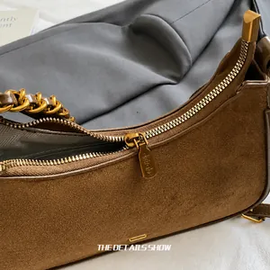 Detalle de bolso de ante marrón con cadena de metal dorado y cremallera grabada