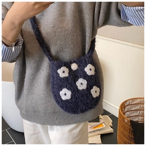 Detail of handcrafted navy blue crochet bucket bag with white flowers and fuzzy pom pom