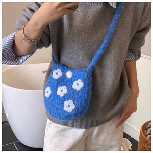 Detail of blue plush knit crossbody bag featuring white 3D flower embroidery and shoulder strap