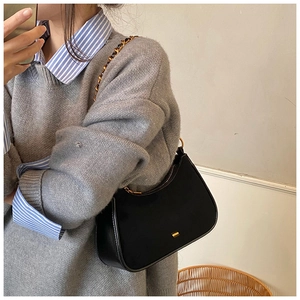 Detalle del bolso de media luna negro minimalista con cadena dorada y adorno metálico