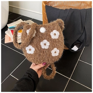 Detail showing the floral embroidery and white fluffy pom-pom on the brown plush bucket bag