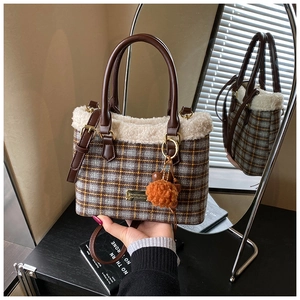 Detail of plaid tote bag with faux shearling trim, orange pom-pom and metal logo plate