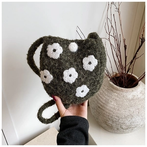 Detail of dark green plush bucket bag featuring white flower embroidery and knit strap