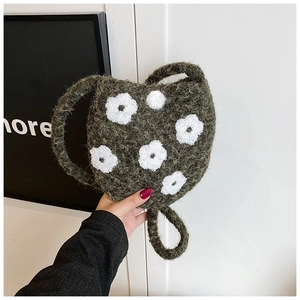 Close-up of dark green plush bucket bag with white floral embroidery and round handles