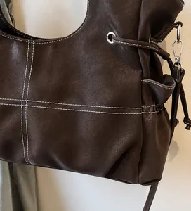Detail of dark brown leather tote featuring white contrast stitching and silver metal hardware