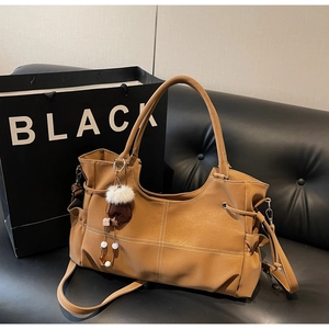 Detail view of large brown leather tote bag with white contrast stitching and soft fur charm