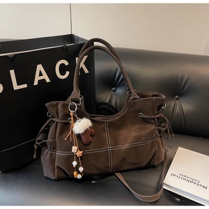 Detail of dark brown leather tote bag with white stitching and plush charms on a sofa