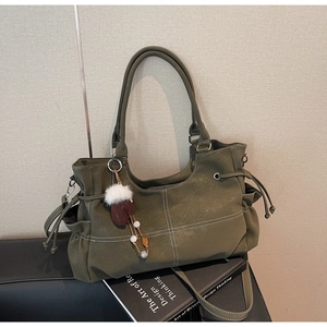 Detail of olive green tote bag featuring white contrast stitching and tassel charm