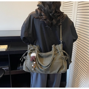 Detail of olive green tote bag featuring drawstring side design and a plush ball charm