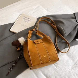 Brown bucket bag with Mugier branding featuring fuzzy ball charms and a long strap