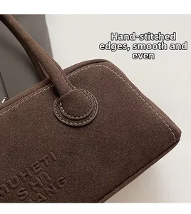 Detailed macro view showing white contrast stitching and embossed text on brown suede bag