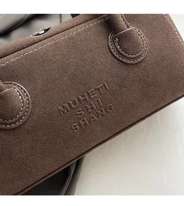 Detailed macro view of the brown suede bag featuring embossed logo and white contrast stitching