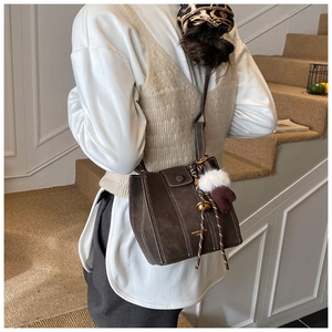Detail of dark brown leather bucket bag featuring white contrast stitching and plush charm