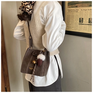 Detail of dark coffee suede bucket bag with contrast stitching and fuzzy charms