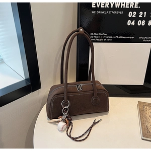 Detail of coffee brown suede bowling bag with baseball charm and dual zipper on white table