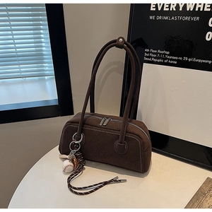 Detailed macro of dark brown suede shoulder bag with contrast stitching and baseball charm