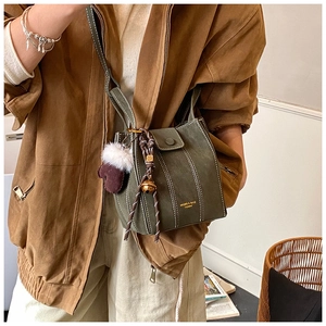 Detail of dark green matte crossbody bag with plush glove charm and woven strap accents
