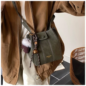Detail of dark green bucket bag with white contrast stitching and a woven bohemian charm