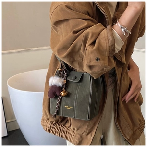 Detail of green suede bucket bag with plush glove charm and golden bell accessory