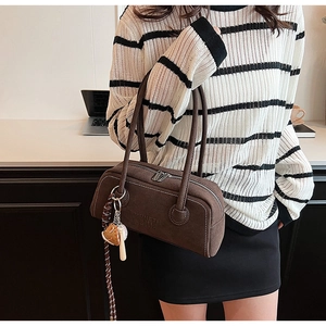 Detail view of a brown suede Boston bag with dual zippers and branding, styled on a model