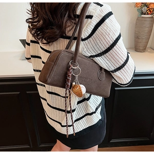Detail of dark brown matte shoulder bag with unique baseball charm and fringe tassel