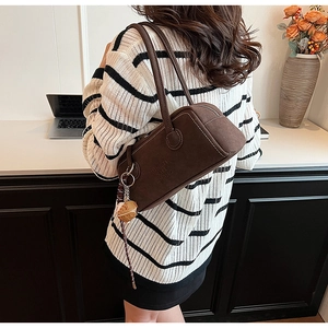 Detailed side view of dark brown frosted suede Boston bag with dice pendant on shoulder