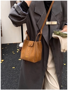 Brown suede bucket bag with white contrast stitching and fuzzy charm on a fashion model