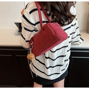 Close-up of a burgundy suede shoulder bag with embossed letters and a strawberry pendant