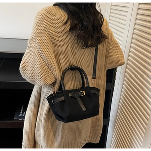 Vista posteriore della modella con borsa a secchiello in tela nera, manici tondi e fibbia