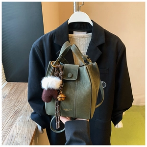 Detail of dark green matte bucket bag with a plush glove charm and magnetic closure