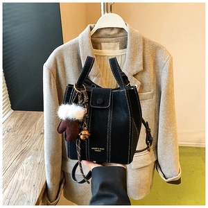 Detail of black bucket bag with white contrast stitching and plush glove charm