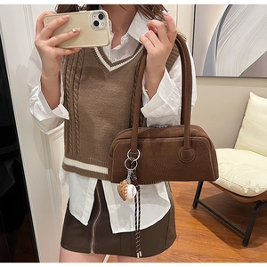 Close-up of brown suede shoulder bag with baseball glove pendant and printed lettering